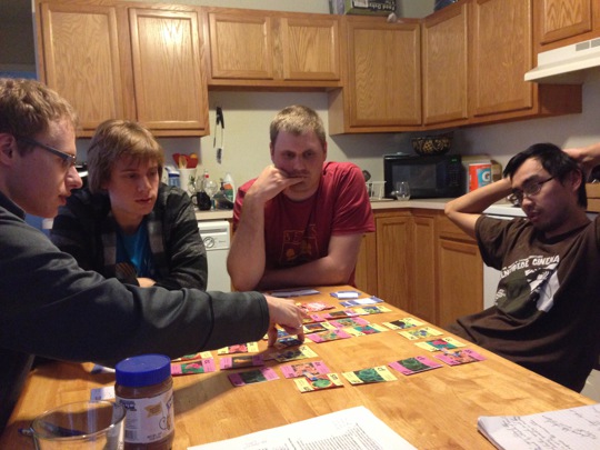 4 players around a table playing the educational card game Conjugation.