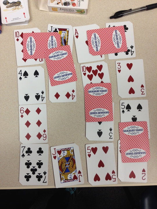 Playing cards on a table arranged in a 4 by 4 grid. Some cards are face down and bridging other cards.