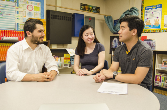 A teacher, parent, and translator having an in-person meeting in a classroom.